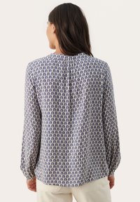 Blus med långa ärmar i lätt material. Har ett mönster av blåa och krämfärgade löv, rundad halsringning och plisserad detalj bak.