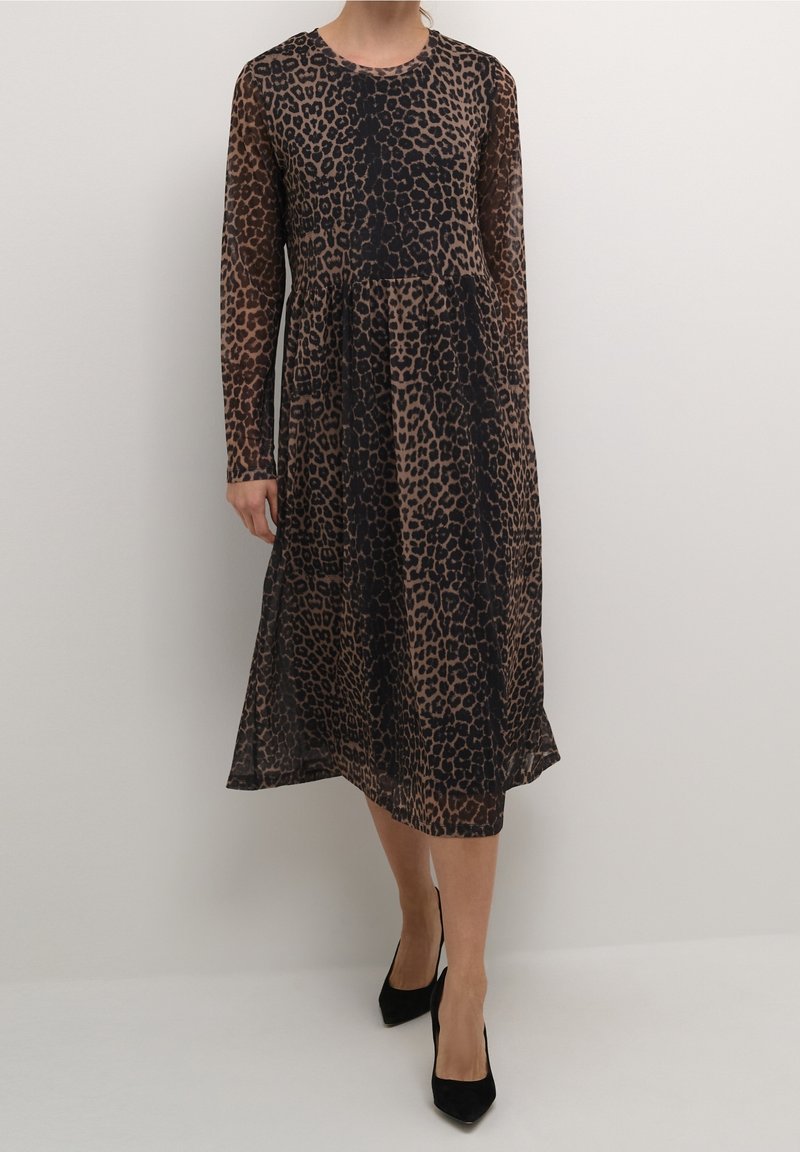 Femme portant une robe à manches longues, longueur mi-cuisse, imprimé léopard marron et noir, associée à des escarpins noirs à bout pointu.