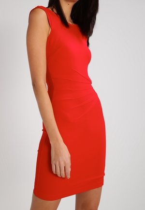 Vestido rojo sin mangas ajustado hasta la rodilla con detalles de costuras asimétricas, llevado por una persona de pie contra un fondo liso.