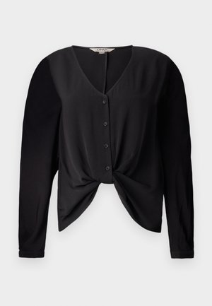 Blouse noire avec un décolleté en V, des manches longues et un devant boutonné. Elle présente un détail de nœud à la taille et une texture de tissu lisse.