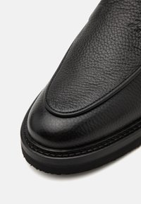 Black leather shoe with a pebbled texture, rounded toe shape, stitching detail along the sole, and a smooth finished heel.