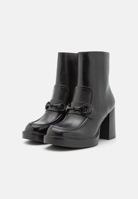 Bottines en cuir noir avec un large talon bloc, dotées d'une sangle décorative et d'une boucle à l'avant, texture lisse.