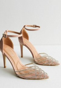 Klart klackar med spetsiga tår, rosa ankelremmar och silverfärgade rhinestones på korskorsremmar. Glänsande finish; smala högklackade.