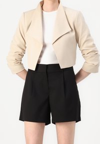 Beige cropped jakke med stor krave, letvægtsstof; kombineret med sort, højtaljede shorts, skræddersyet pasform, glat tekstur.