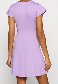 Lila kortärmad klänning med figursydd överdel och utsvängd kjol. Tillverkad av mjukt, stretchigt tyg med subtila sömdetaljer på baksidan.