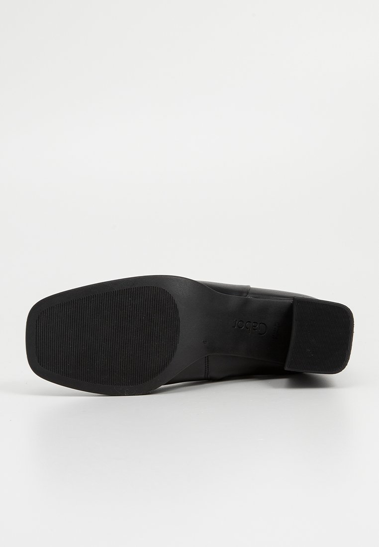 Fekete cipő sima bőrből készült felsőrésszel és texturált gumitalppal. Alacsony sarka és a talpon lévő vésett logó jellemzi.