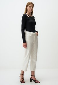 Maglietta nera a manica lunga con una texture a coste e scollatura sulla spalla, abbinata a jeans bianchi a gamba dritta e sandali neri con cinturini.