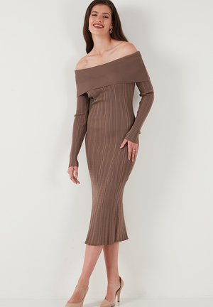 Brown ribbed off-shoulder midi dress with long sleeves, fitted silhouette, and subtle texture, paired with nude high-heeled shoes.