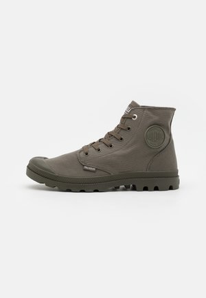Botte montante en toile vert olive avec semelle en caoutchouc, fermeture à lacets à l'avant et écusson rond du logo à la cheville.