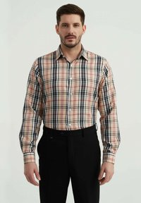 Chemise à boutons à carreaux beige, noir, rouge et blanc. Manches longues, col standard, avec une coupe ajustée. Pantalons noirs en dessous.