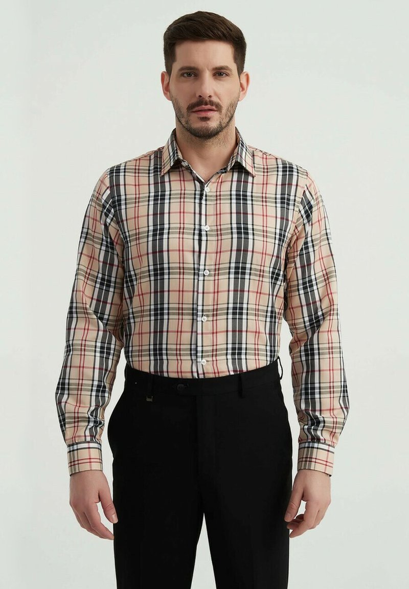 Chemise à boutons à carreaux beige, noir, rouge et blanc. Manches longues, col standard, avec une coupe ajustée. Pantalons noirs en dessous.