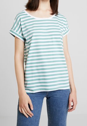 Woman wearing a green and white horizontal striped short-sleeve T-shirt with rolled sleeves and blue jeans against a plain background.