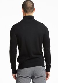 Črna pulover s turtleneck ovratnikom, dolgimi rokavi, oprijetim krojem, fino pleteno teksturo ter rebrastim ovratnikom in robom, v kombinaciji s sivo hlačami.