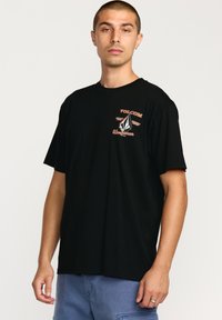 Sort bomulds T-shirt med korte ærmer, prydet med et frontlogo i orange og hvid, afslappet pasform og rund halsudskæring.