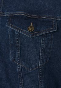 Denimová košile v tmavě modrém odstínu, s náprsní kapsou s kulatým klopou, zlatým knoflíkem a viditelným prošíváním.