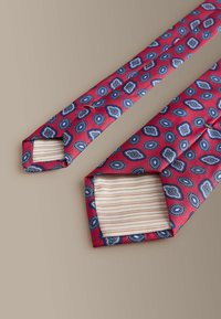 Sarkana kaklasaite ar zilām ovāla un kvadrāta motīvēm. Ir teksturēta auduma un svītrainas iekšējās apdares, kas redzama uz galiem.