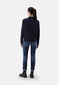 Navy long-sleeve shirt with a collar, paired with blue jeans and black ankle boots. Features a straight back and button cuffs.