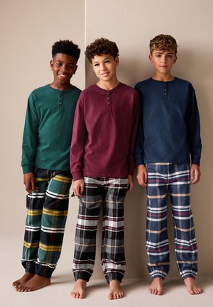Drie jongens dragen loungewear: groene, bordeauxrode en marineblauwe tops met lange mouwen en knoopdetails; geruite broeken in verschillende kleuren met elastische boorden.