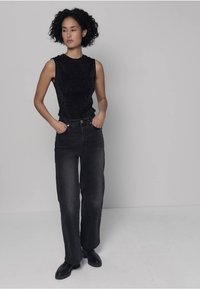 Musta, hihaton toppi, jossa hienovarainen tekstuuri, yhdistettynä korkeavyötäröisiin, suoralahkeisiin mustiin farkkuihin ja mustiin kenkiin. Yksinkertainen ja moderni muotoilu.