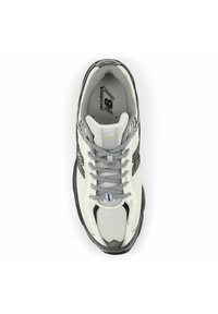 Vita och grå mesh-sneakers med grå skosnören och ett mönstrat gummisul; har en framträdande "N"-logotyp på sidan och en vadderad krage.