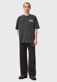 Mørkegrå oversized t-shirt med logo foran, kombineret med sorte vidde bukser og sorte sko, med metal-kædedetalje på bælte.