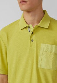 Limonkowa koszulka polo z teksturowanej tkaniny, z zapięciem na trzy guziki, żebrowanym kołnierzykiem i kieszonką na lewej stronie.
