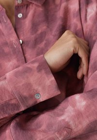 Chemise à manches longues dans une teinte rose dégradée, avec un tissu doux, une fermeture à boutons et un poignet avec un subtil détail de bouton.