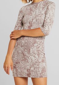 Lyhythihainen, sovitettu mekko vaaleanbeigellä pohjalla, jossa on vaaleanpunainen käärmeennahkakuosi. Pehmeä, joustava kangas, jossa korkea pääntie ja helma, joka on yli reiden puolivälin.