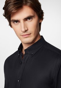 Czarna koszula z guzikami, posiadająca strukturalny kołnierzyk, charakteryzująca się delikatną teksturą, kontrastowymi guzikami oraz slim fit.