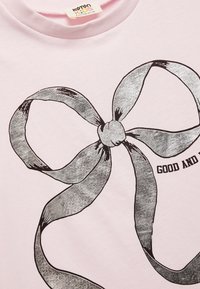 Lyserød bomulds T-shirt med et stort, sølvmetallic buegrafik med sorte kanter og teksten "GOOD AND". Blød, glat tekstur.