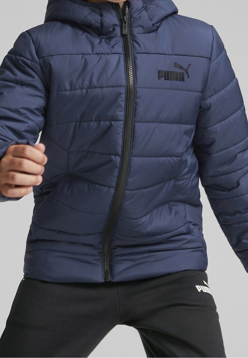 Granatowa kurtka puchowa z zamkiem błyskawicznym z przodu, pikowaną teksturą i kapturem. Wyposażona w czarne logo Puma na piersi oraz czarny zamek.