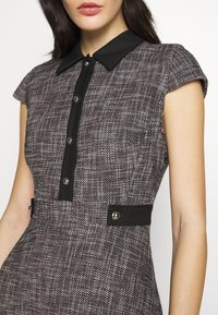 Sukienka z krótkim rękawem w fakturowanej tkaninie w czerwono-bordowym i szarym kolorze, z czarnym kołnierzem, guzikiem z przodu i czarnymi akcentami w talii.