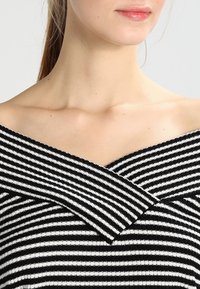 Top scollato con strisce orizzontali bianche e nere, caratterizzato da un'ampia scollatura piegata e un tessuto morbido e testurizzato.