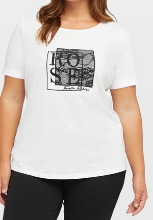 Woman wearing white short-sleeve shirt with black lace square and large black text reading "ROSE" on front, paired with black pants.