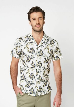 Korte mouwen overhemd van witte stof met een bloemmotief in donkerblauw en groen. Voorzien van een reverskraag en een losse pasvorm.