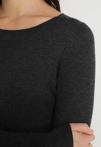 Maglione a maglia grigio scuro con scollatura ampia e maniche lunghe. Texture morbida con polsini a costine, caratterizzato da un design semplice e classico.