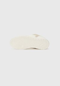 Sneaker sole in cream color, featuring a textured rubber material with a geometric pattern. Accents in light beige near the upper.