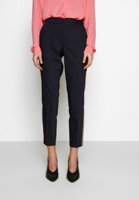 Námořnické kalhoty s úzkým střihem a zúženými nohavicemi, s kontrastními oranžovými pruhy na bocích. Vyrobené z hladké tkaniny, stylizované s skrytým předním zapínáním.