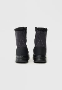 Μαύρες χειμερινές μπότες με επενδυμένο εξωτερικό, κολάρο από συνθετική γούνα και αντίθετη ραφή. Η σόλα εί�ναι επίπεδη με ανάγλυφο σχέδιο πρόσφυσης.