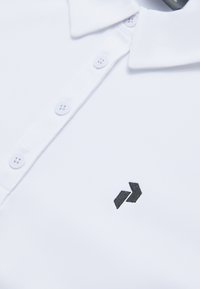 Witte poloshirt met een kraag, voorzien van een zwart geborduurd logo op de borst en een vijfknopenplacket met witte knopen.