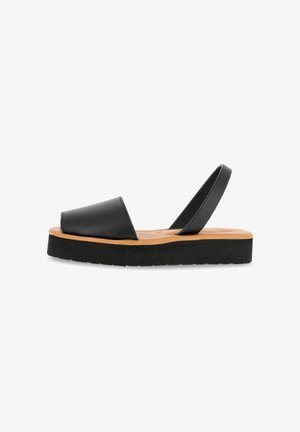 Black leather slingback sandal with a wide toe strap, beige footbed, and a thick black rubber sole. Minimalist design with clean lines.