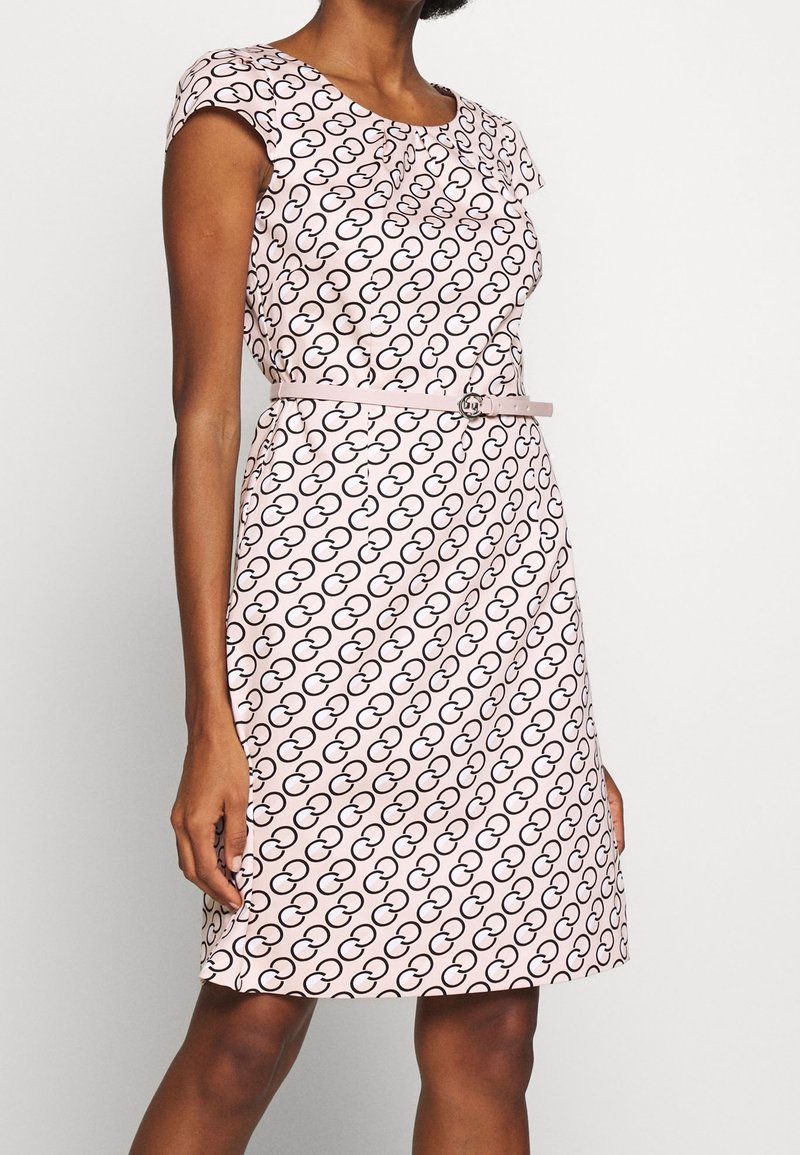 Robe rose avec un motif circulaire noir répétitif, des manches courtes, une coupe ajustée et une ceinture fine assortie avec une boucle ronde.