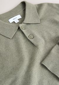 Olijfgroene poloshirt gemaakt van zachte stof met een kraag, twee knopen en geribbelde manchetten, met een gladde textuur en een subtiel ontwerp.