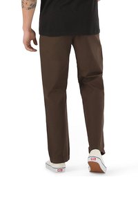 Pantaloni di cotone marroni con taglio dritto, tasche laterali e orlo con risvolto, indossati con scarpe bianche senza lacci dotate di suola texturizzata.