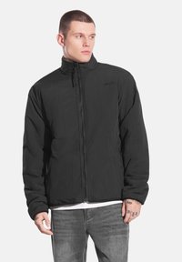 Czarna kurtka zapinana na zamek z wysokim kołnierzem, wykonana z lekkiego materiału. Posiada zapinane na zamek boczne kieszenie oraz teksturowaną powierzchnię.