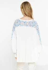 Maglione bianco con un retro leggero a fantasia floreale in tonalità di blu e beige; vestibilità oversize con maniche ampie e scollatura rotonda.