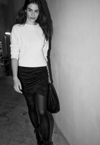 Czarna marszczona spódnica z srebrnymi ćwiekami, w połączeniu z białym swetrem. Do tego czarne rajstopy i botki za kostkę. Prosta torebka na jednym ramieniu.