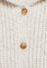 Tissu en maille épaisse couleur crème avec deux grands boutons ronds marron, mettant en valeur la texture détaillée et le placement des boutons sur un vêtement.