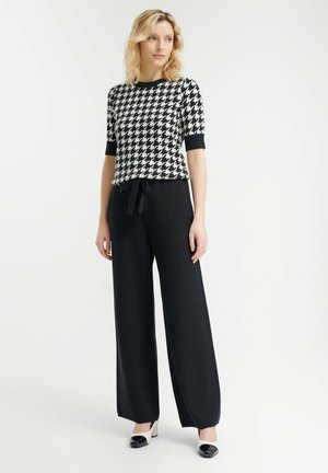 Zwart-wit houndstooth-patroon top met korte mouwen, gecombineerd met hoge zwarte wijde broeken en zwarte hakken.