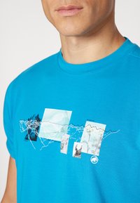 Camiseta de manga corta turquesa con estampados gráficos, que incluyen formas abstractas e imágenes de vida salvaje, con una textura sutil.